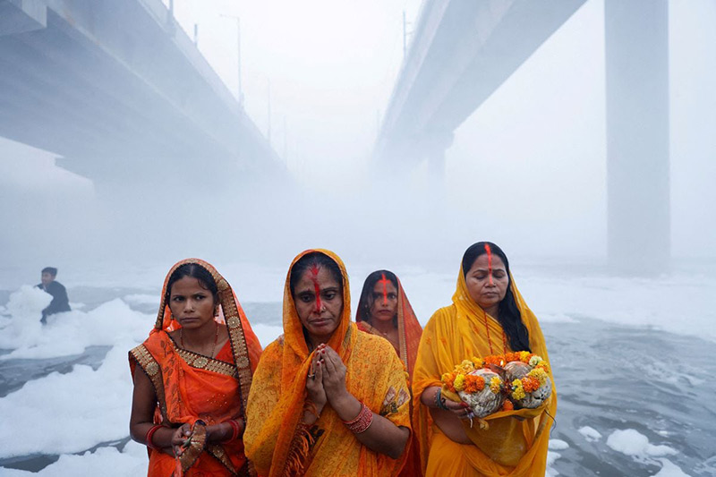 ایستادن فداییان خدای خورشید در رودخانه‌ای آلوده و کف آلود در هند