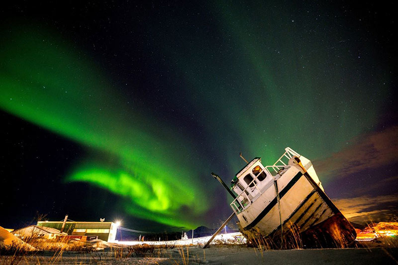 شفق قطبی بر فراز یک قایق در ساحلی در نروژ