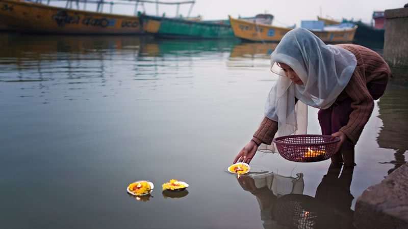زن هندی در حال انداختن بسته‌های گل روی آب