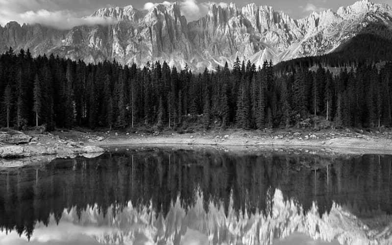 عکس سیاه و سفید از دریاچه ای در کنار جنگل و کوهستان برفی