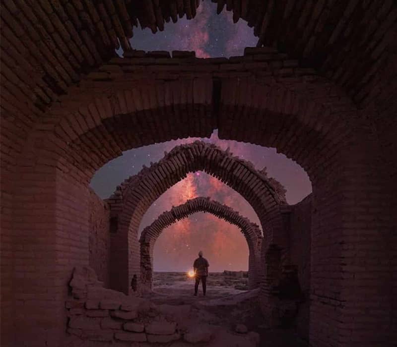 مردی چراغ به دست در کنار بقایای سازه ای تاریخی در شب