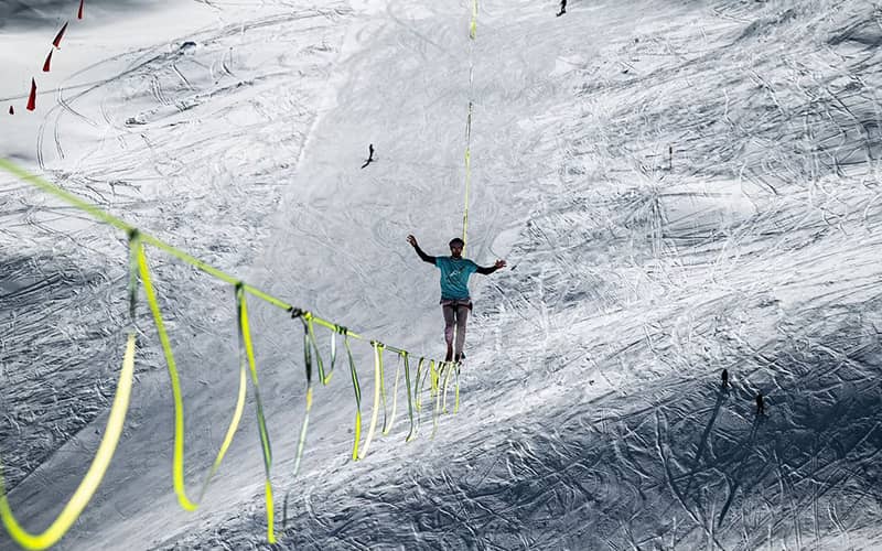 بندبازی در حال راه رفتن روی طنابی در منطقه ای کوهستانی و برفی