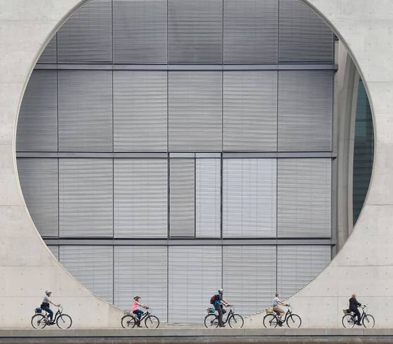 عبور دوچرخه سوارها از کنار ساختمانی با یک دایره بزرگ