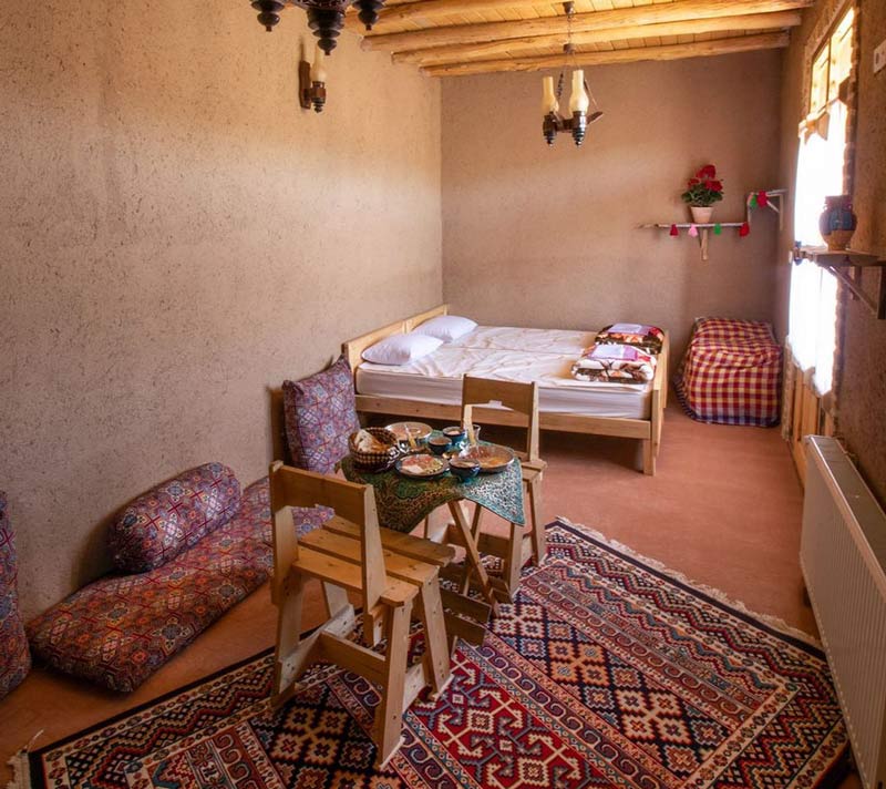 نمایی از تخت و نیمکت های چوبی در اتاق کاهگلی اقامتگاه بومگردی زشک زیبا