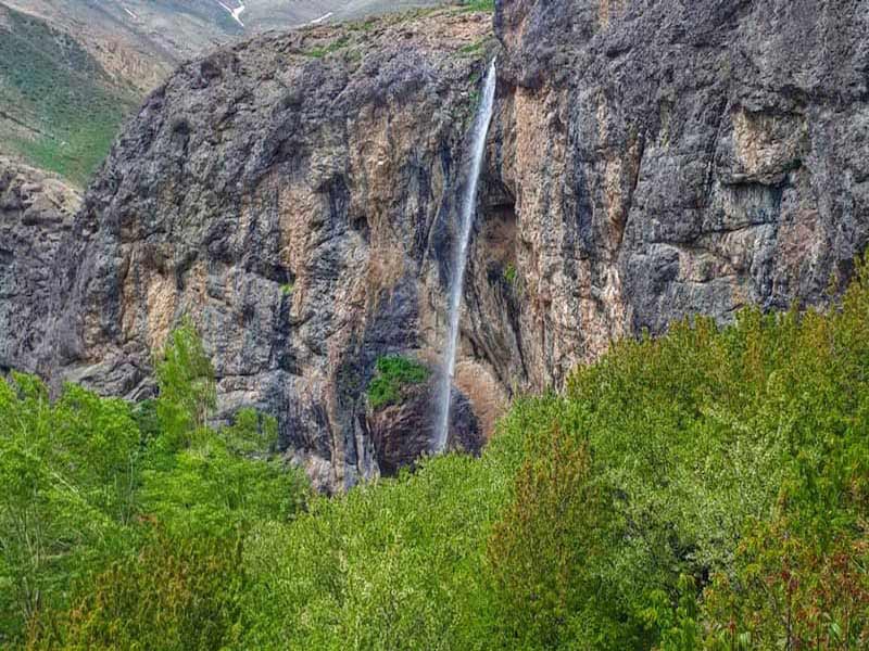 چشم انداز آبشار سنگان میان صخره های بلند و درختان سبز