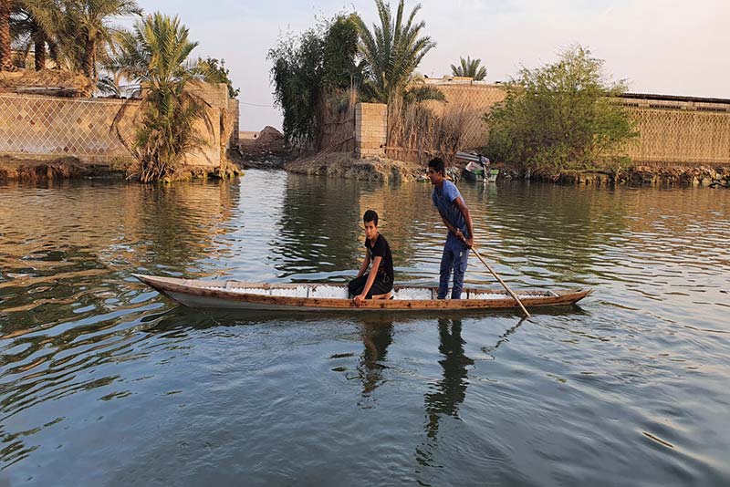 دو جوان روستایی قایق سوار در حال گذر از آب؛ منبع عکس: mehr news؛ عکاس: قاسم منصور آل کثیر