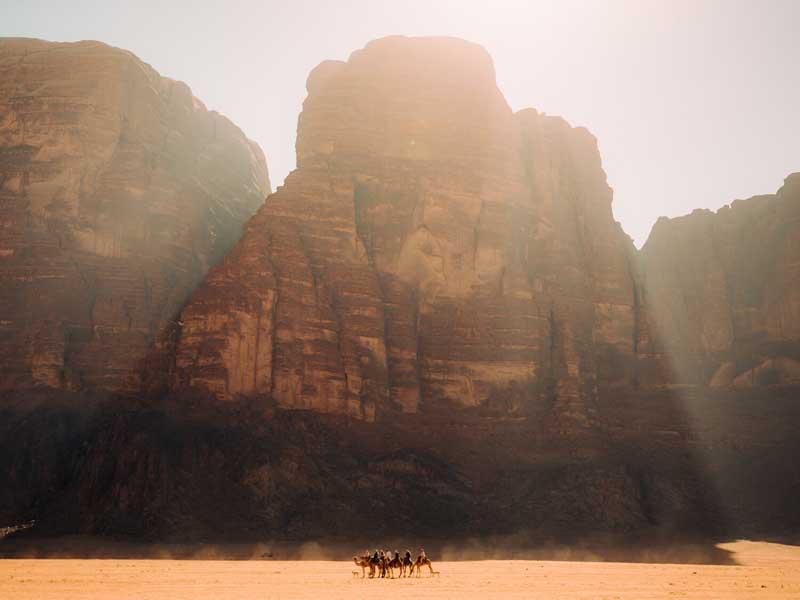 عبور چند شتر سوار از جلوی صخره‌ای در صحرای اردن