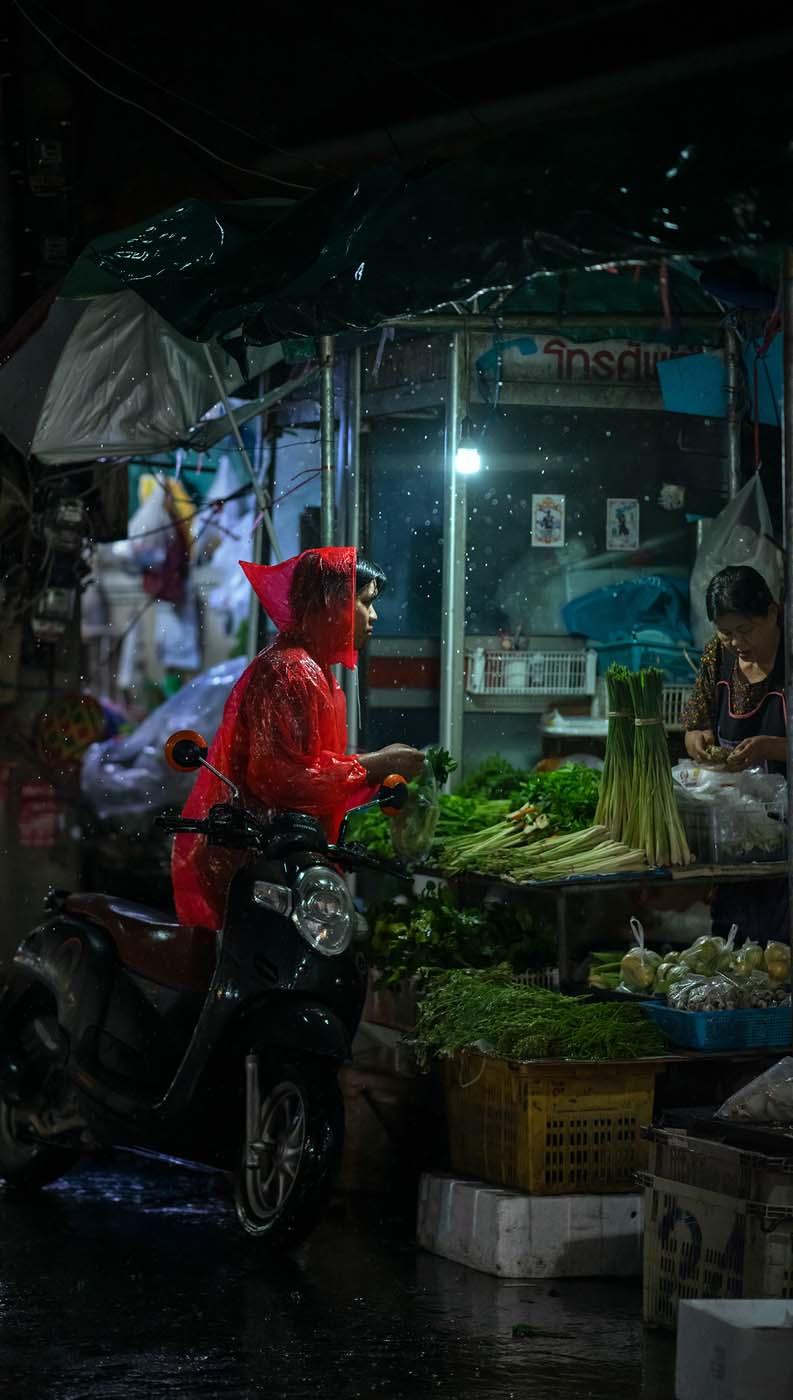 زنی در حال خرید سبزیجات در خیابان بارانی شهر چیانگ مای