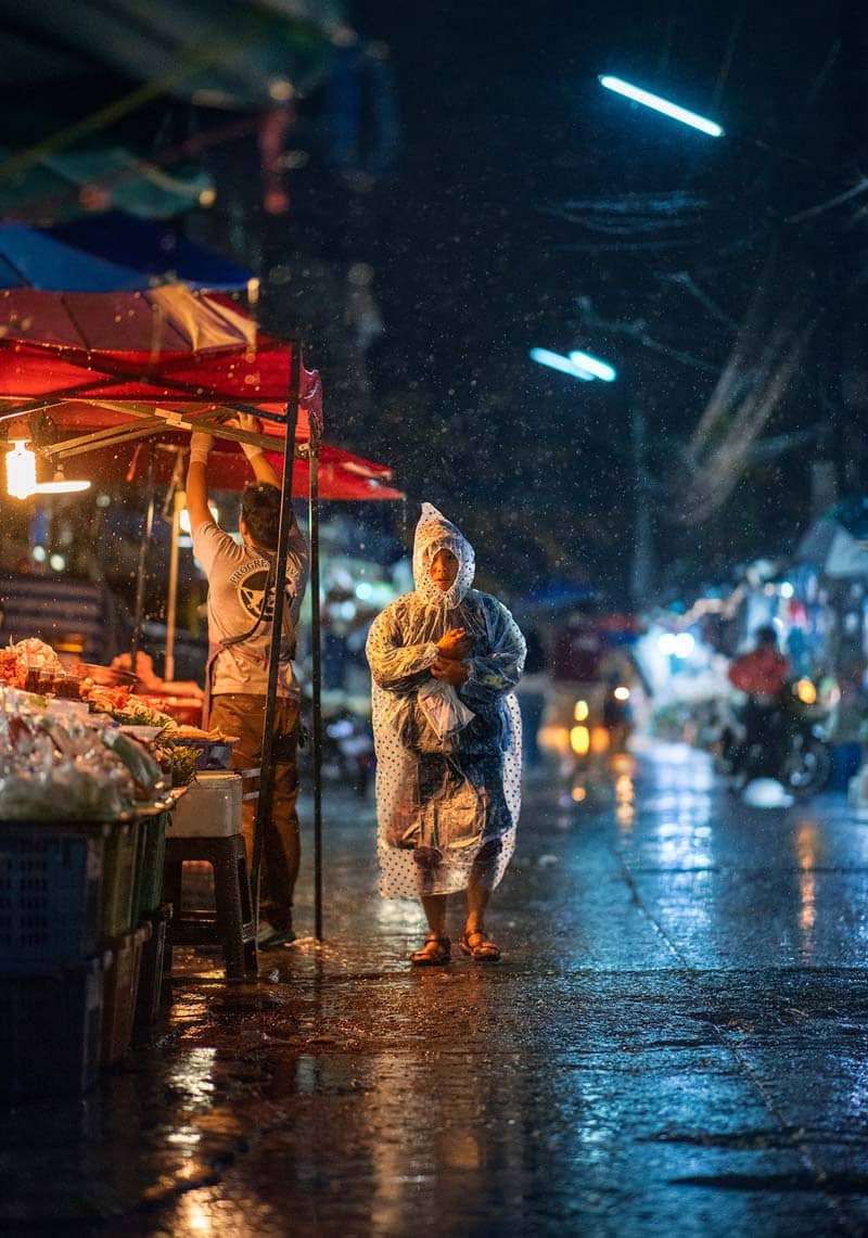 زنی با کاور ضد آب در خیابان بارانی شهر چیانگ مای در شب