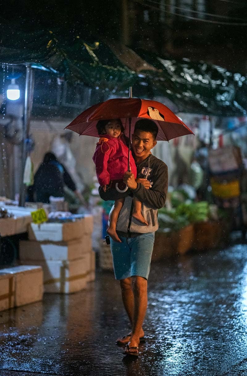 مردی به همراه کودکش و یک چتر در خیابان بارانی شهر چیانگ مای