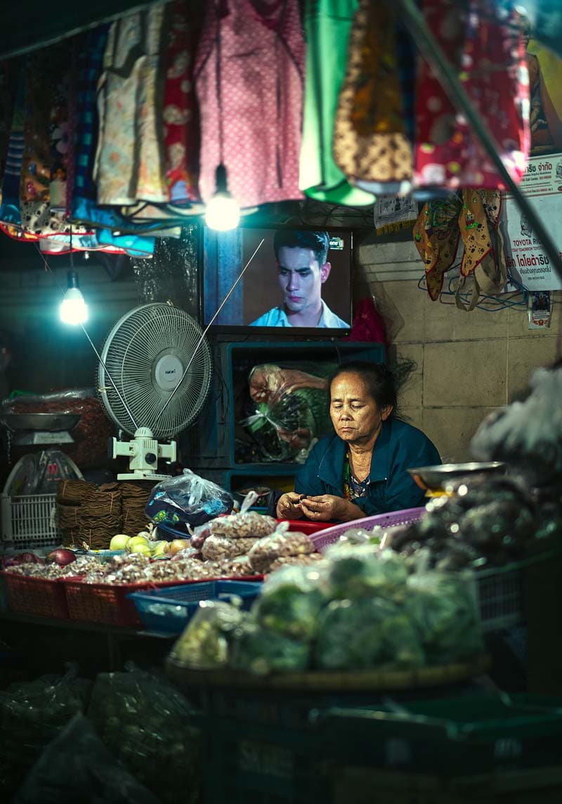 زن فروشنده نشسته در غرفه‌ای خیابانی در تایلند
