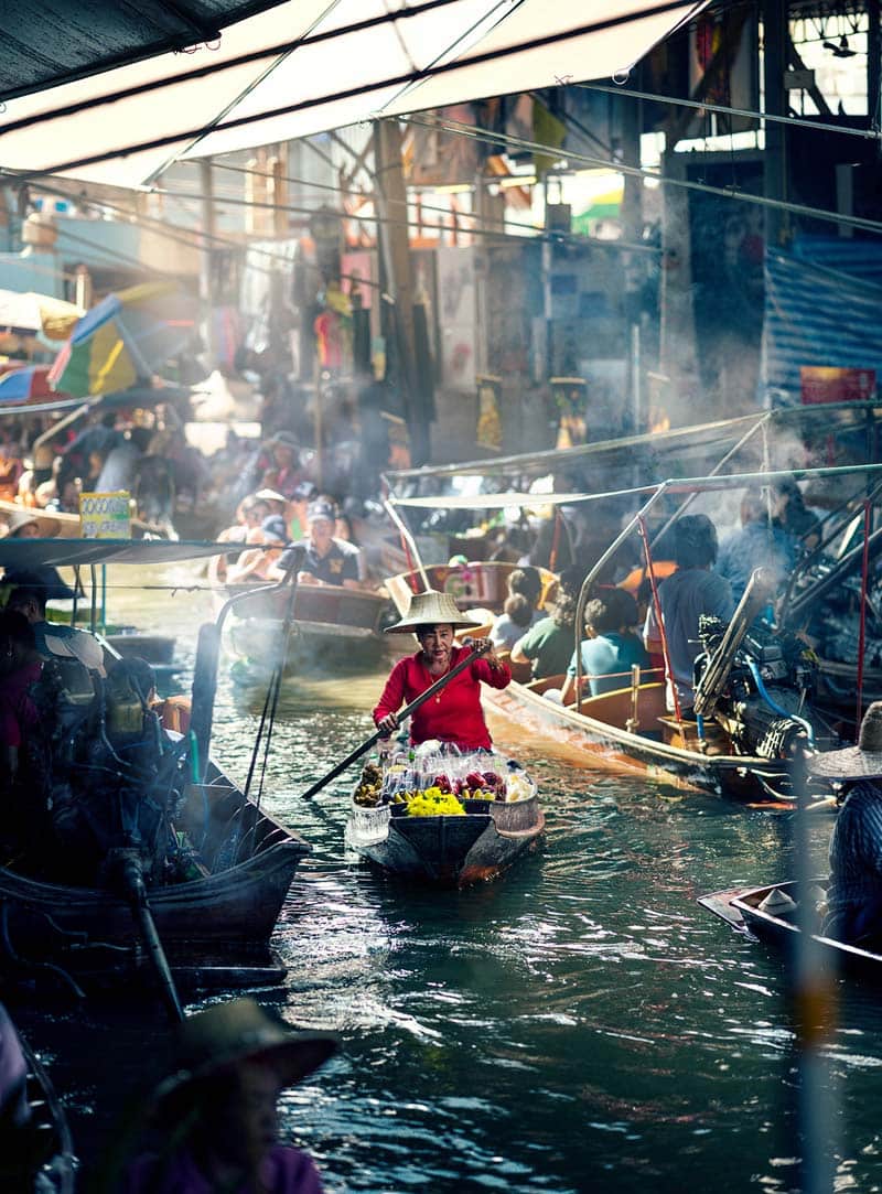 زن فروشنده قایق سوار تایلندی در حال پارو زدن در رودخانه