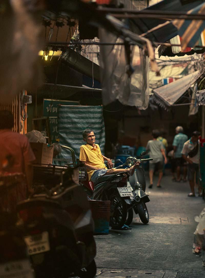 مردی نشسته بر موتور در کوچه‌ای باریک در تایلند