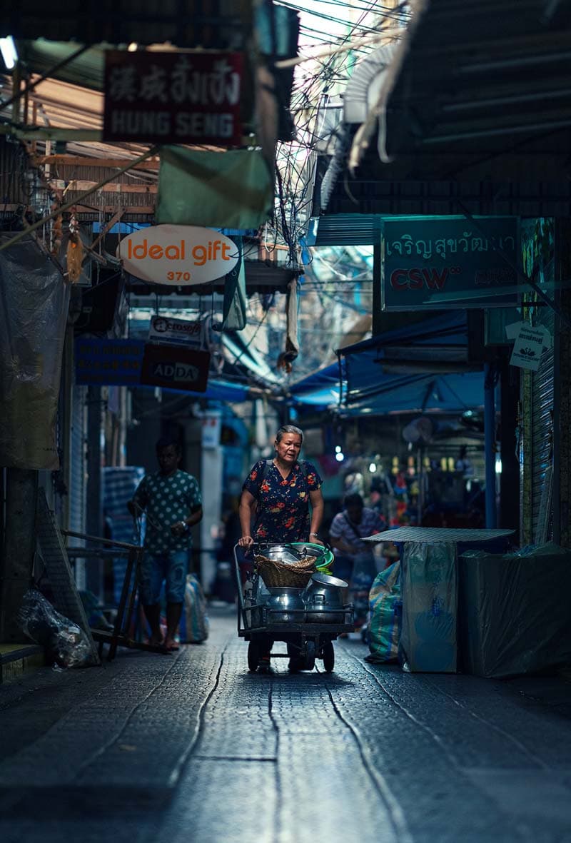 زنی با چرخ دستی وسایل در حال عبور از خیابانی در شهر بانکوک