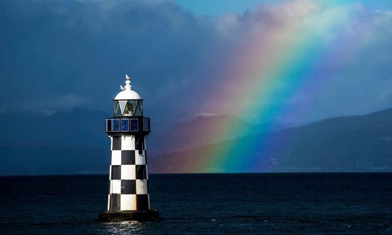 طاق رنگین کمانی در آسمان و پشت فانوس دریایی در اینورکلاید (Inverclyde) اسکاتلند