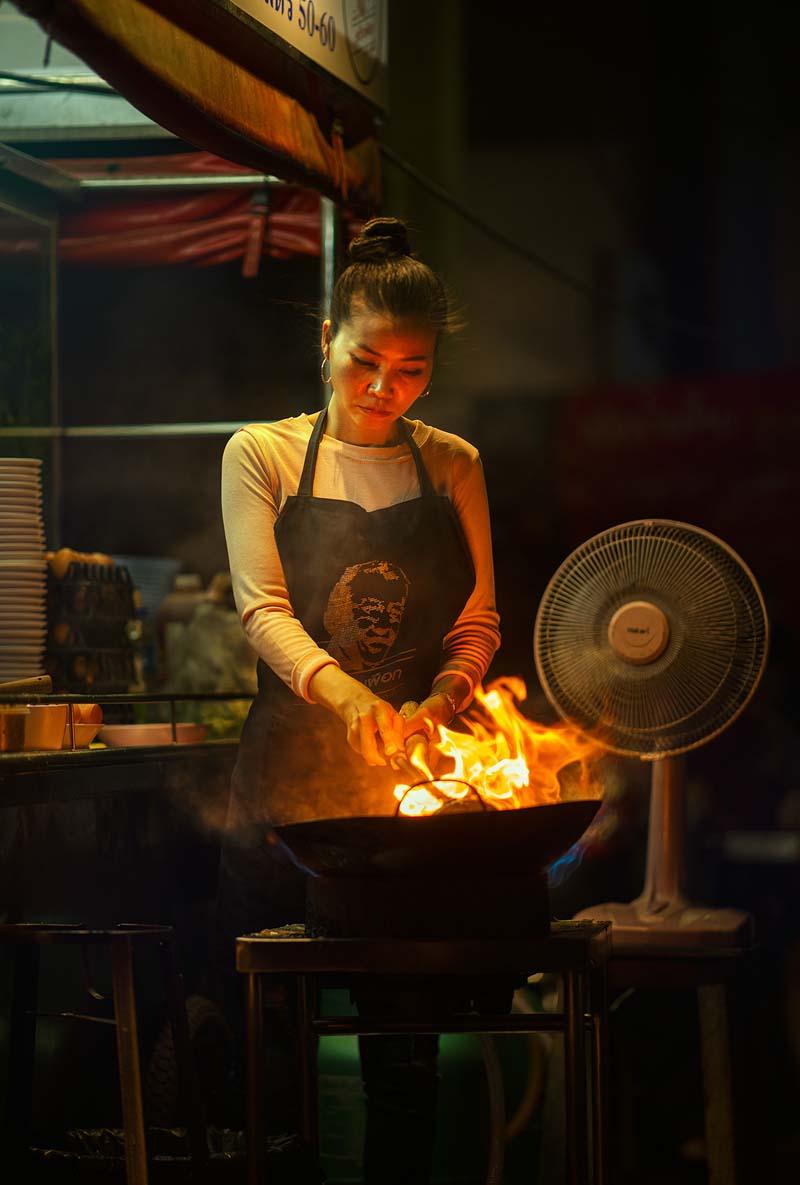 دختری در حال آشپزی در کافه‌ای خیابانی در شهر چیانگ مای