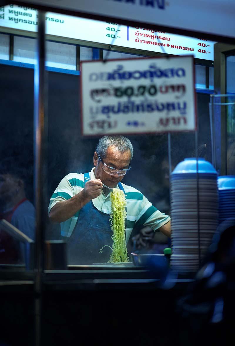 مرد تایلندی در حال پخت نودل در غرفه خیابانی