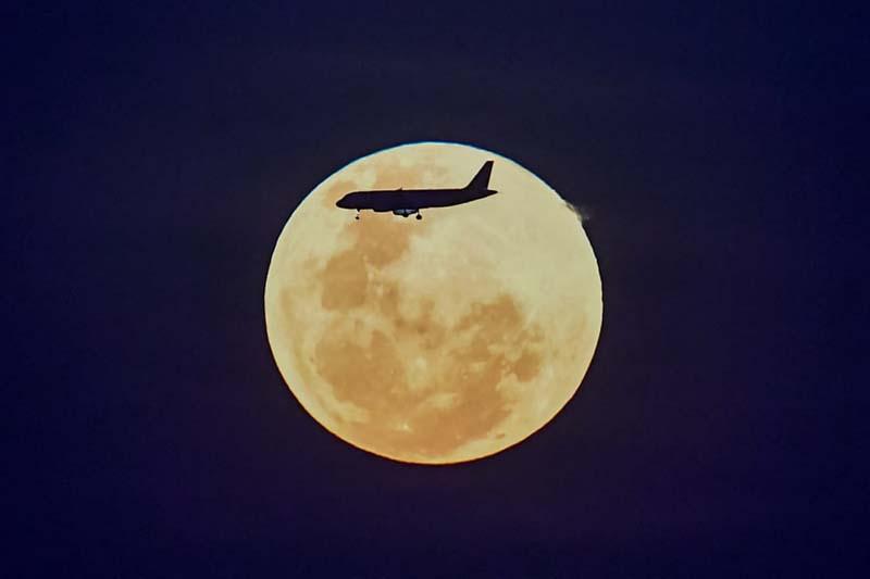 یک هواپیما از کنار ماه کامل در حال طلوع در سنگاپور می گذرد