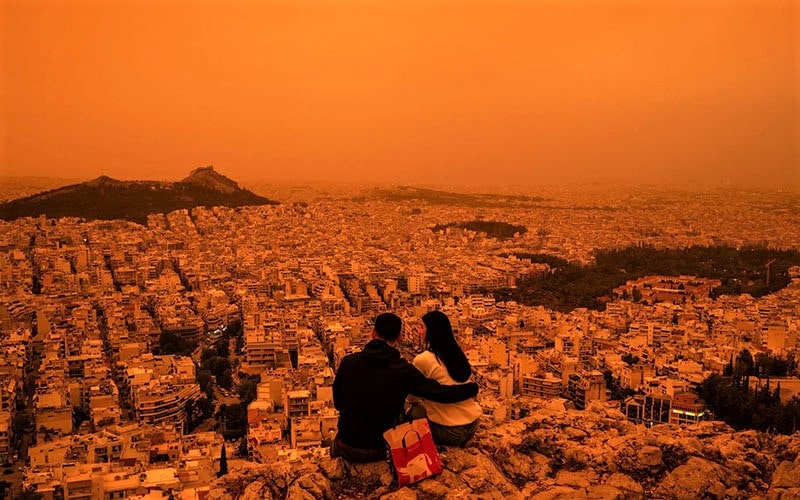 زوجی در حال تماشای شهر آتن به رنگ نارنجی، منبع عکس: Getty Images، عکاس: Angelos Tzortzinis 