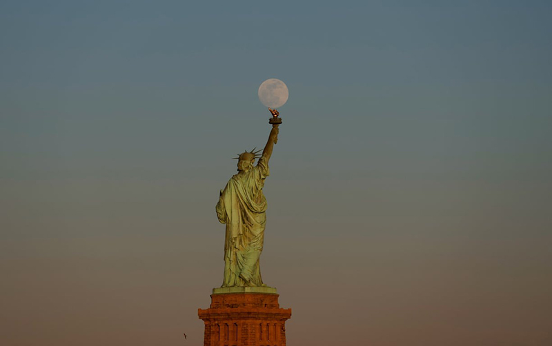 طلوع ماه از پشت مجسمه آزادی در نیویورک؛ منبع عکس: Getty Images؛ نام عکاس: Gary Hershorn