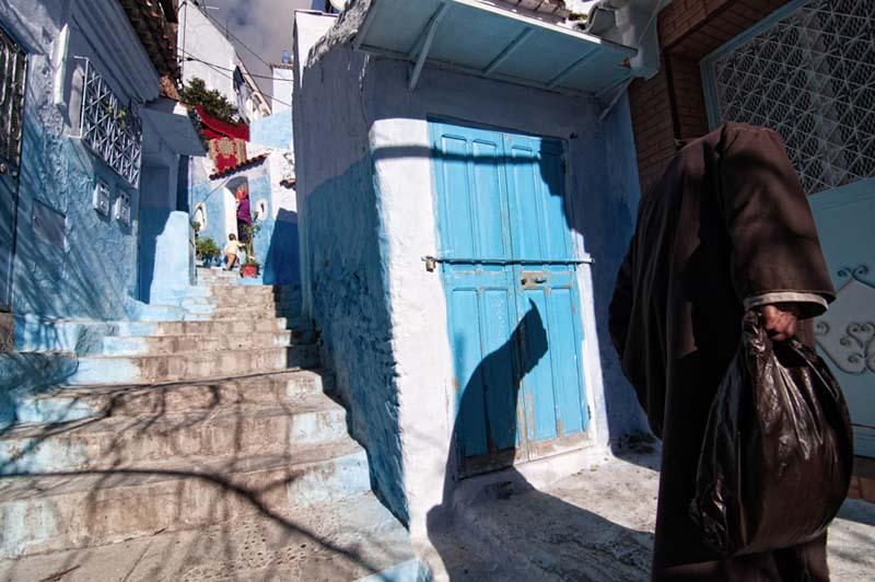 فردی با یک کیسه در دست در کوچه ای پلکانی و آبی رنگ در مراکش