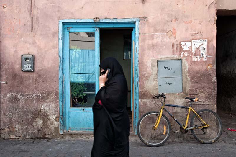 عبور زن چادری تلفن به دست از مقابل یک درب آبی رنگ در مراکش